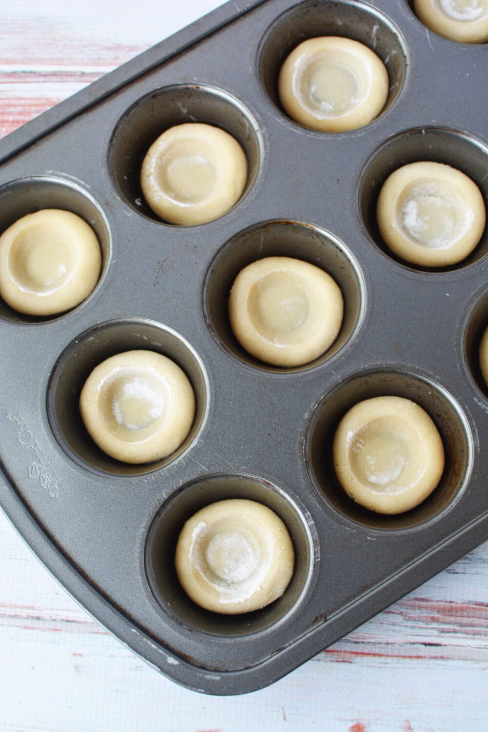 Cookie dough shaped into crusts in a muffin pan. 