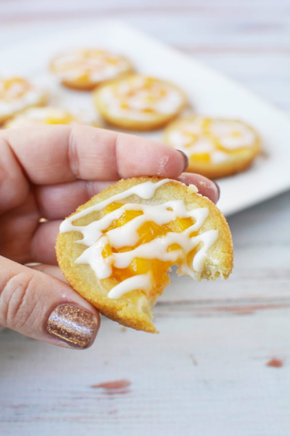 Holding a peach pie sugar cookie with a bite missing.