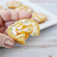 Holding a peach pie cookie with a bite missing.