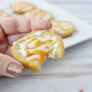 Holding a peach pie cookie with a bite missing.