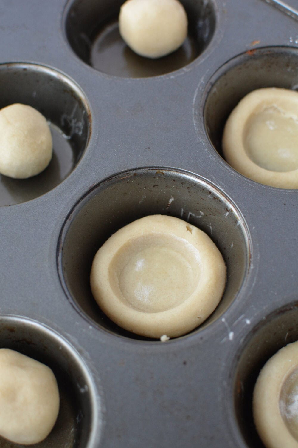 Cookie dough shaped into little pie crusts in a muffin tin.