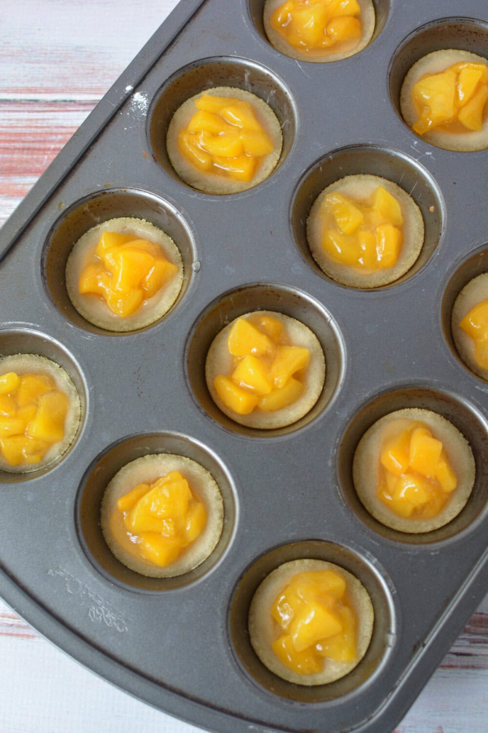 Sugar cookie crusts filled with peach pie filling ready to be baked.