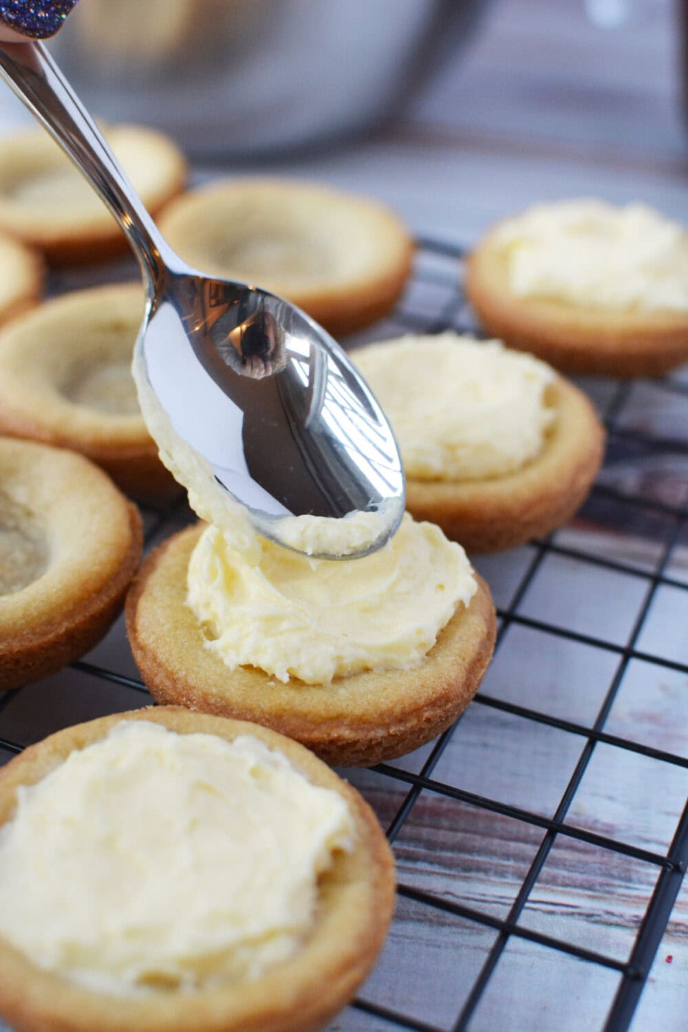 Using a spoon to add custard filling to mini sugar cookie pie crusts.