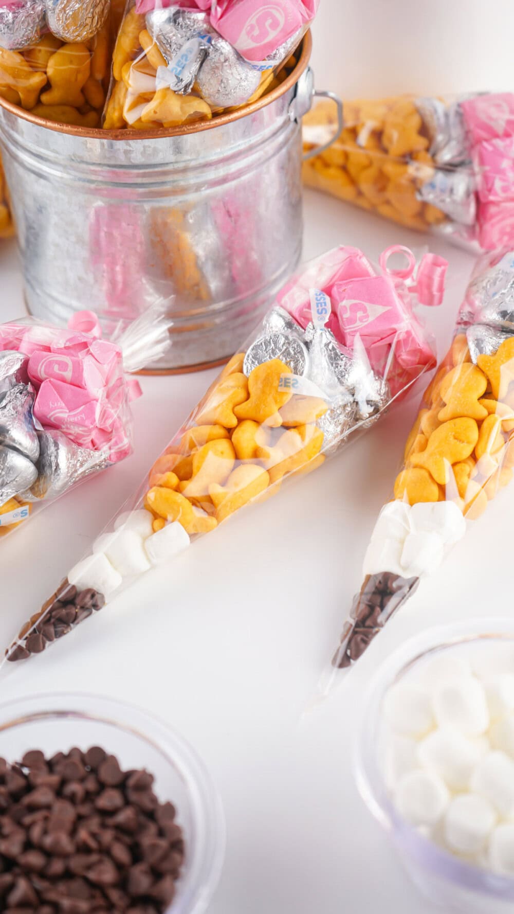 Snack bags that look like a pencil on a table next to a bucket. 