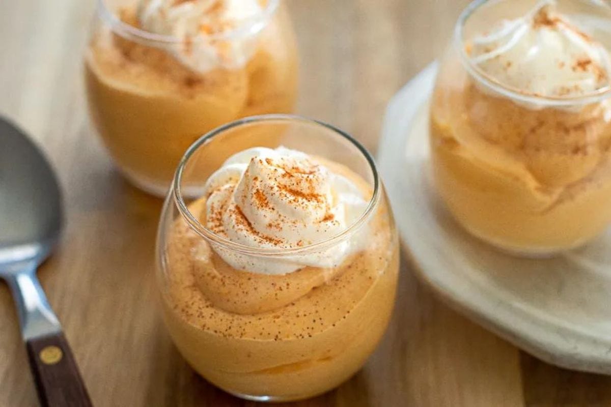 Pumpkin pie mousse in glasses topped with whipped cream.