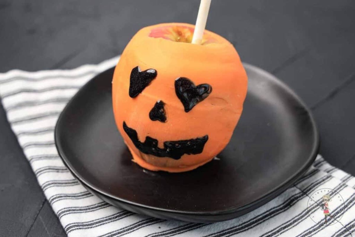 Candy apple with a pumpkin face on it.