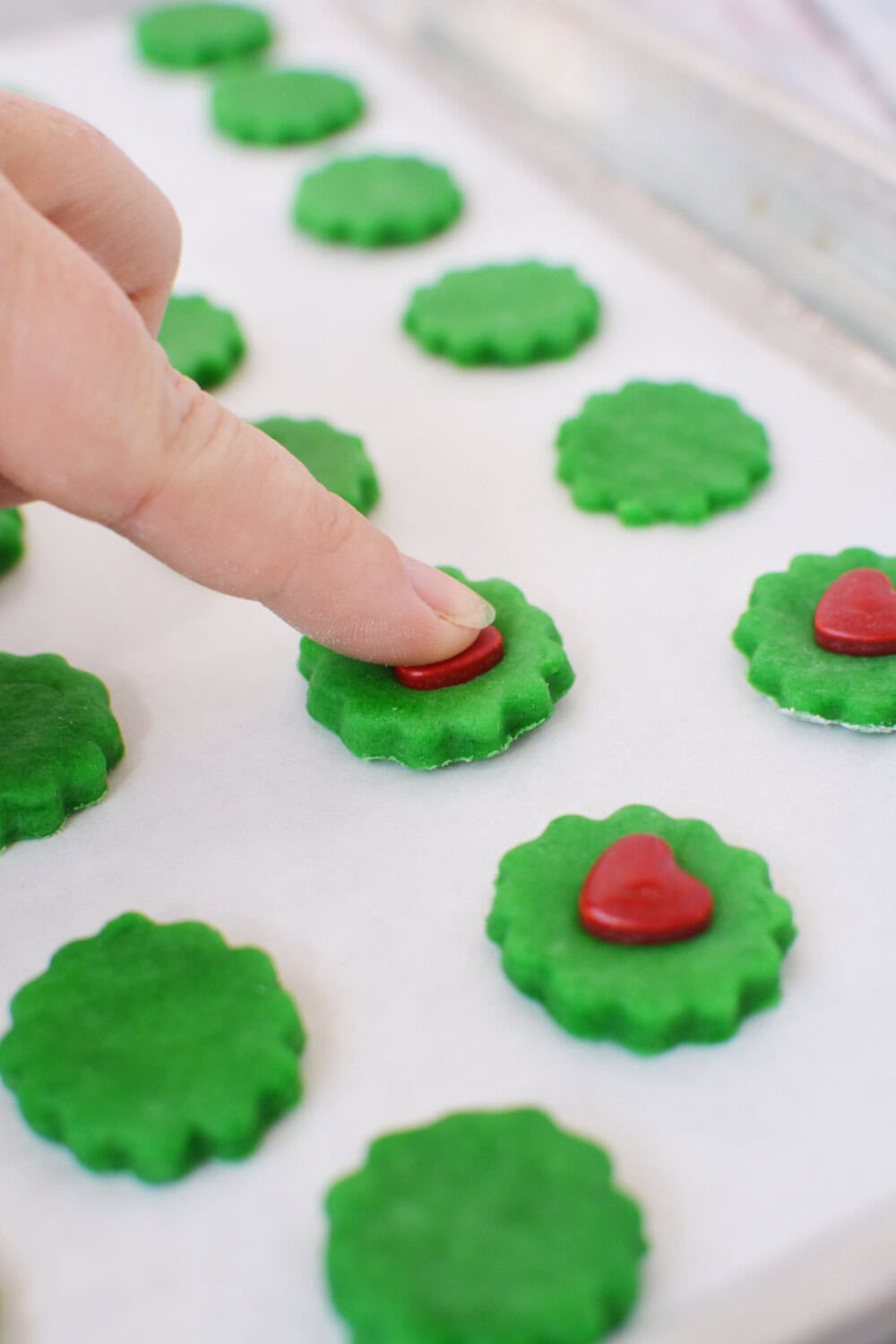 Pressing red heart candies into green dough.