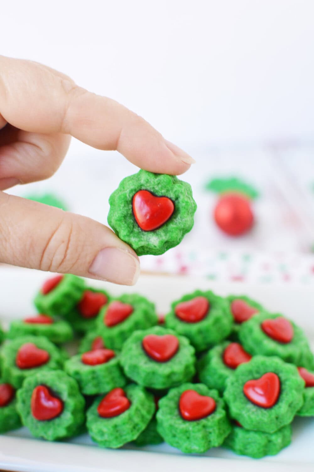 Holding a Grinch shortbread bite above the plate full of them.