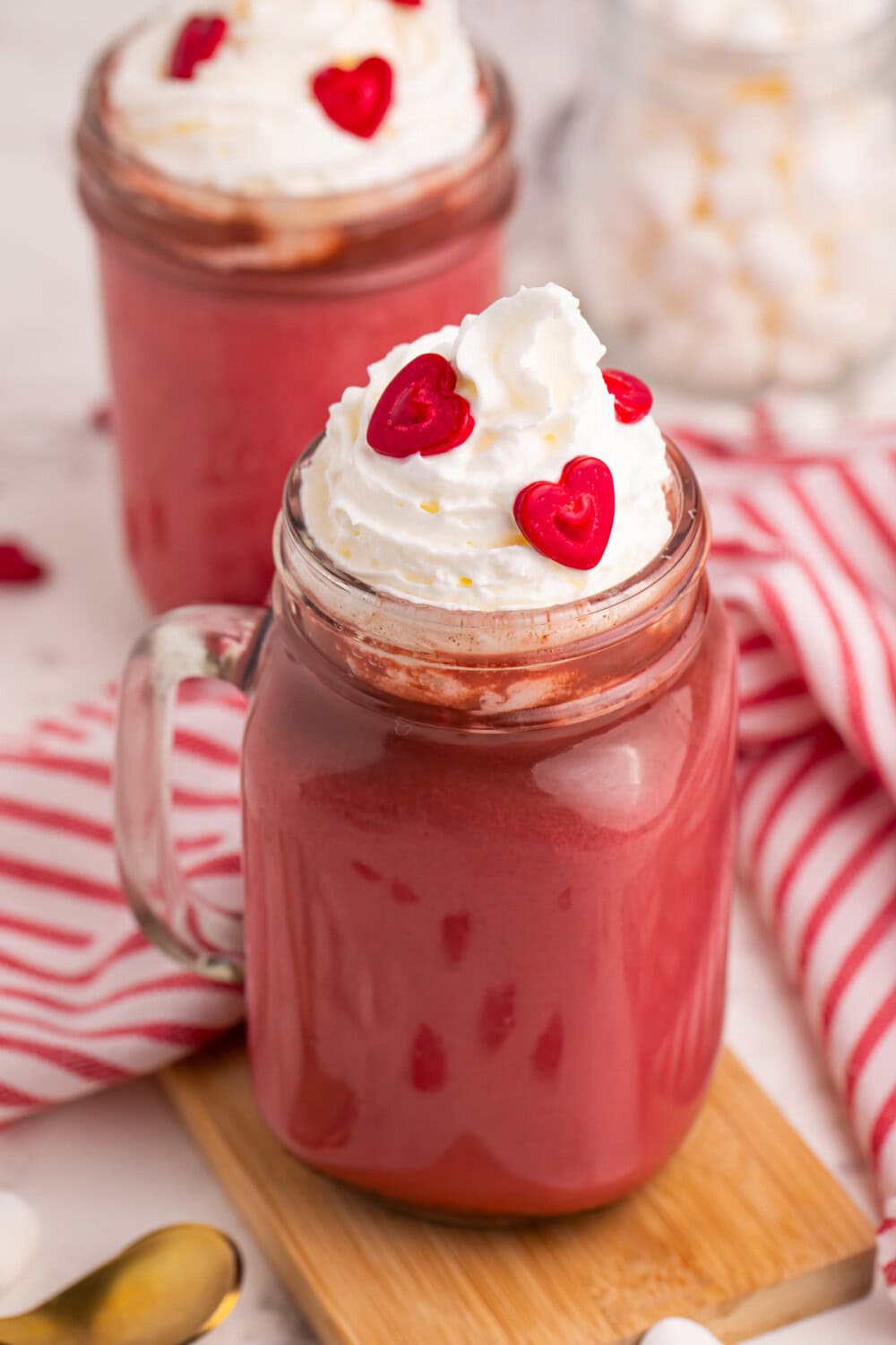 Red chocolate drink in a jar with whipped cream and heart sprinkles.
