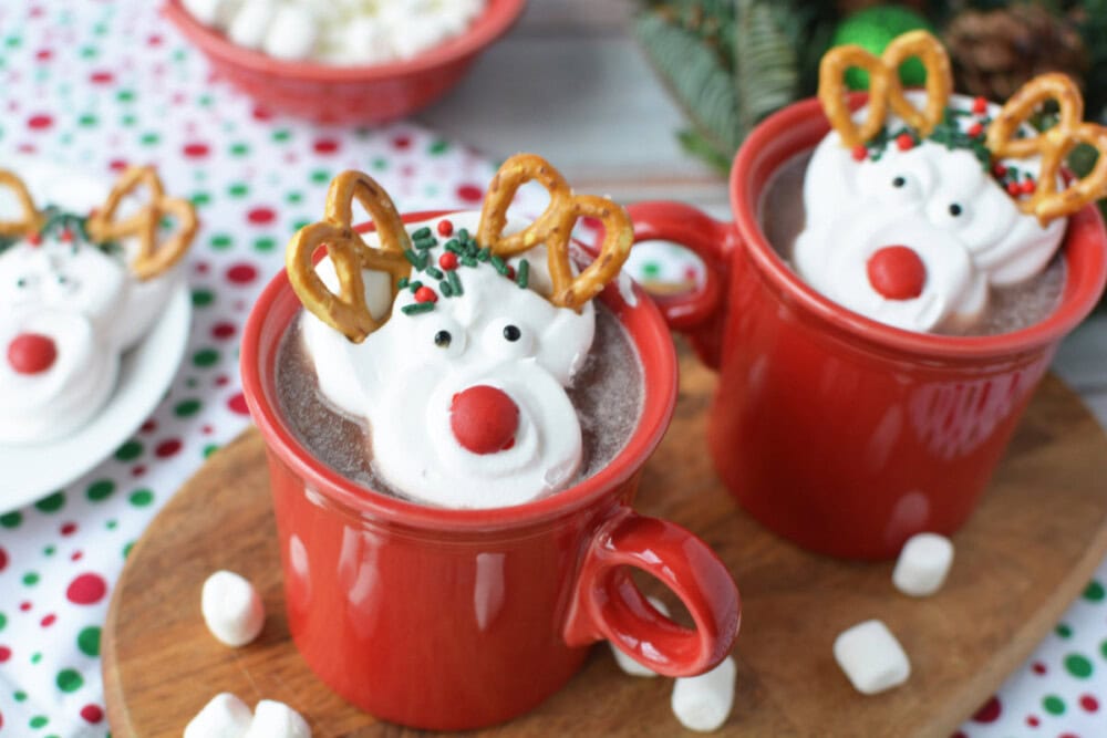 Two mugs of hot cocoa topped with reindeer whipped cream