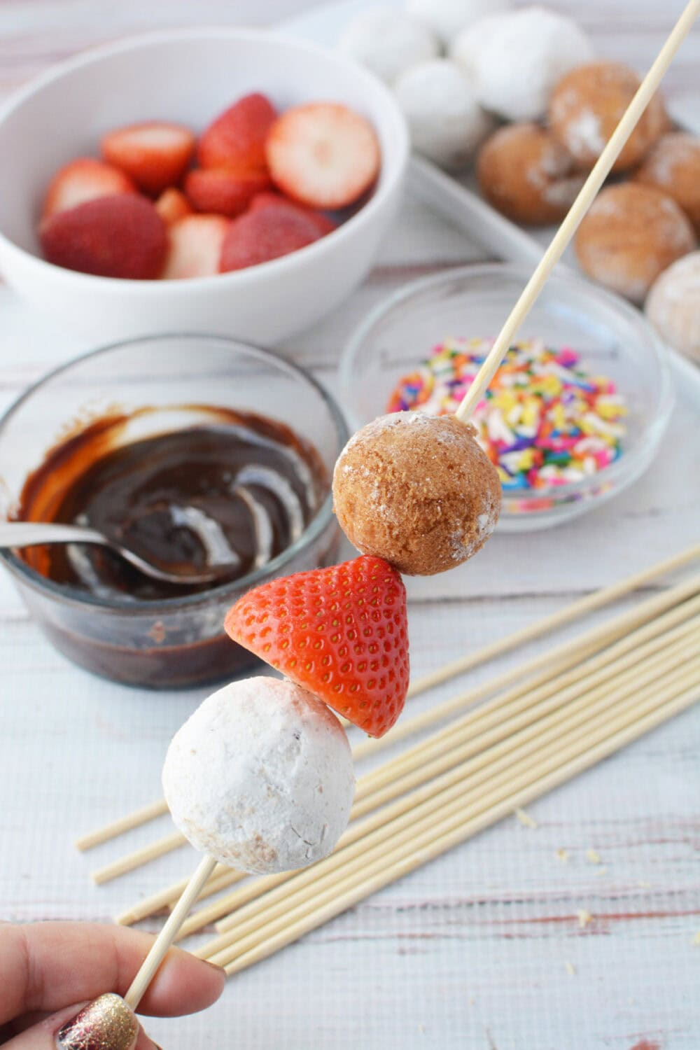 Two donut holes and a strawberry on a skewer.