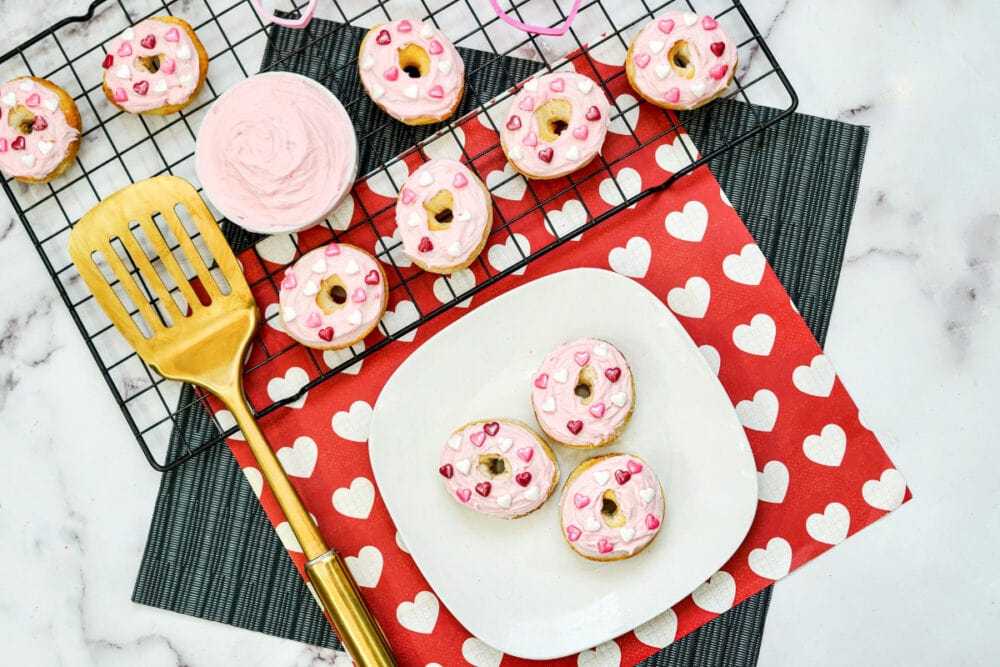 Strawberry mini donuts with Valentine's sprinkles on a plate and a cooling rack.