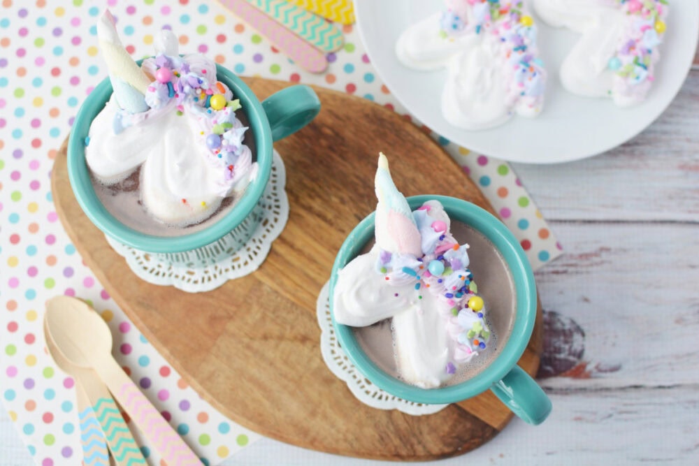 Two unicorn whipped cream toppers in mugs of hot chocolate.